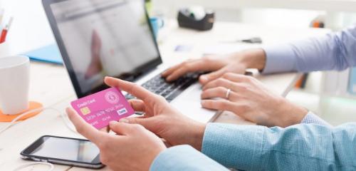 różowa karta kredytowa w dłoniach w tle osoba dokonująca zakupu przez laptopa