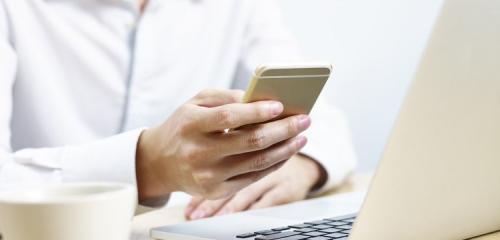 kobieta w białej koszuli siedząca przed laptopem z telefonem w dłoni