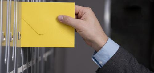 męska dłoń wsuwająca żółtą kopertę do skrzynki na listy