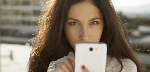 kobieta spoglądająca zza białego smartfona