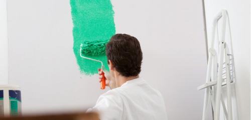 mężczyzna malujący wałkiem ścianę na zielony kolor