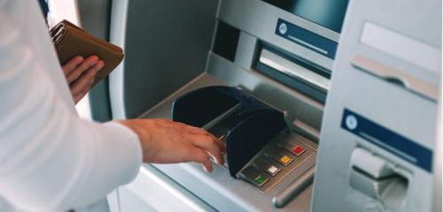 osoba w białej koszuli wypłacająca gotówkę z bankomatu