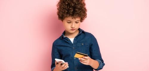 chłopiec z kartą kredytową i telefonem komórkowym na różowym tle