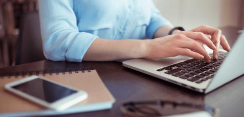 kobieta w niebieskiej koszuli pisząca na klawiaturze laptopa