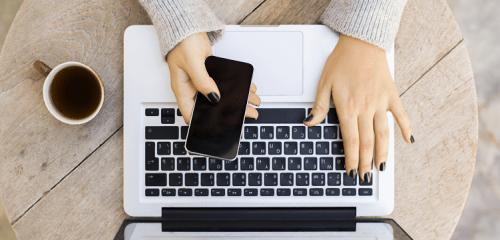 kobieta ze smartfonem i laptopem siedząca przy stole i starająca się zaciągnąć kredyt na PESEL