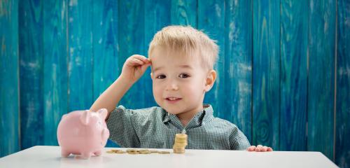Małe dziecko ze świnką skarbonką i monetami na stole
