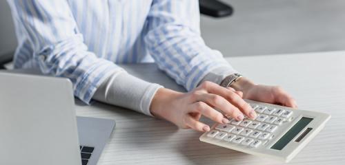 Kobieta siedząca przy laptopie i obliczająca na kalkulatorze debet na koncie bankowym