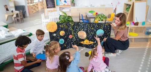 Dzieci siedzą na podłodze w przedszkolu i uczą się przez zabawę o kosmosie