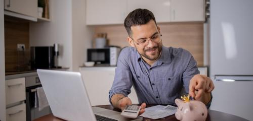 mężczyzna siedzący przy stole z laptopem i świnką skarbonką sprawdzający ranking pożyczek na 800 zł