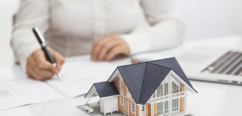 kobieta na tle modelu domu podpisuje umowę o kredyt hipoteczny