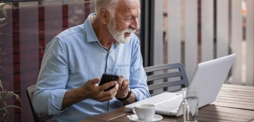starszy mężczyzna siedzący w kawiarni i sprawdzający jak wypłacić pieniądze z ppk