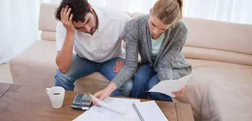 zmartwiona para mająca problem ze spłatą kredytu siedzi nad stertą papierów i kalkulatorem
