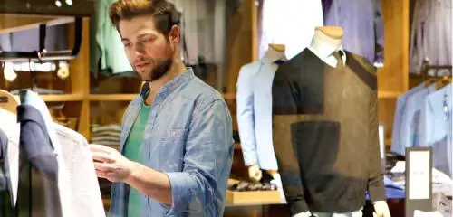 młody mężczyzna oglądający koszulę w sklepie
