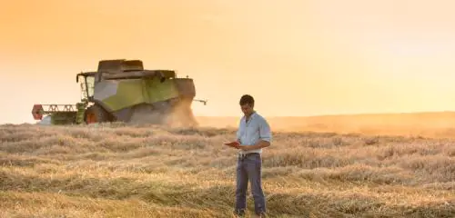 mężczyzna na polu zboża w tle kombajn