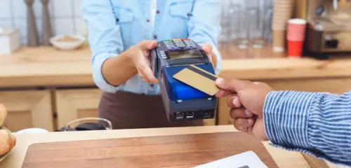 mężczyzna w kawiarni przykładający kartę kredytową do terminala