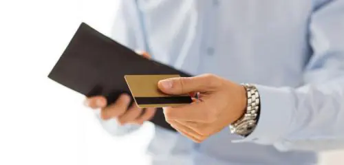 mężczyzna w błękitnej koszuli trzymający w jednej dłoni portfel a w drugiej kartę kredytową