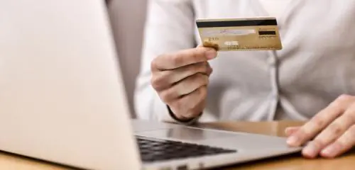 kobieca dłoń trzymająca złotą kartę kredytową nad otwartym laptopem