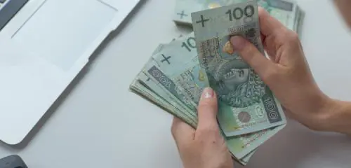 kobiece dłonie trzymające nad biurkiem plik stuzłotowych banknotów