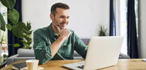 zadowolony mężczyzna siedzący przed komputerem i sprawdzający numer iban swojego konta