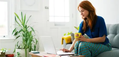 kobieta siedząca na sofie i sprawdzająca na laptopie swój debet na koncie bankowym