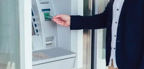 Mężczyzna wkłada do bankomatu kartę płatniczą